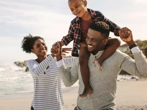 Mother and father walking on beach with son on father's shoulders
