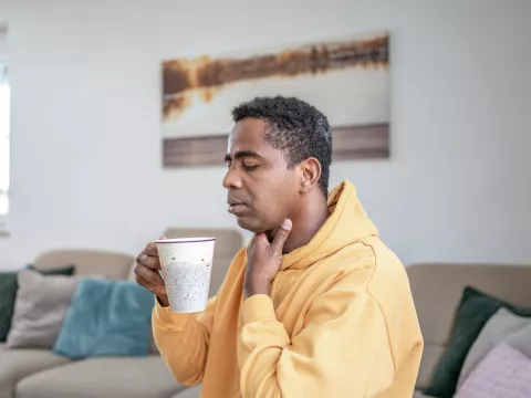 A man with a sore throat sips a cup of hot tea.