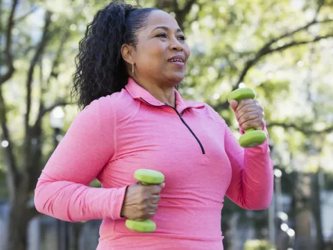 Woman walking outdoors and carrying small hand weights