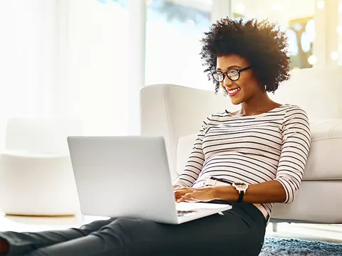 African American woman with glasses working on her laptop.