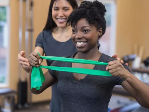 Woman stretching a resistance band with help from a rehab professional