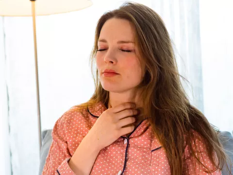 Woman touching her sour throat while sitting at home while wearing pajamas.