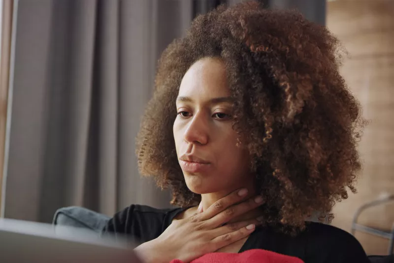 A woman touching her throat and showing discomfort