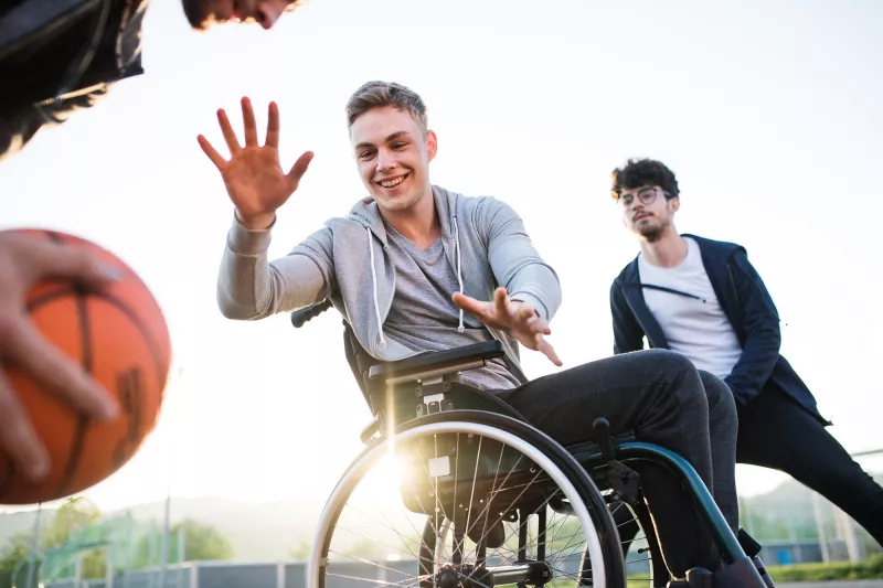 Older teens playing basketball one of which is in a wheelchair