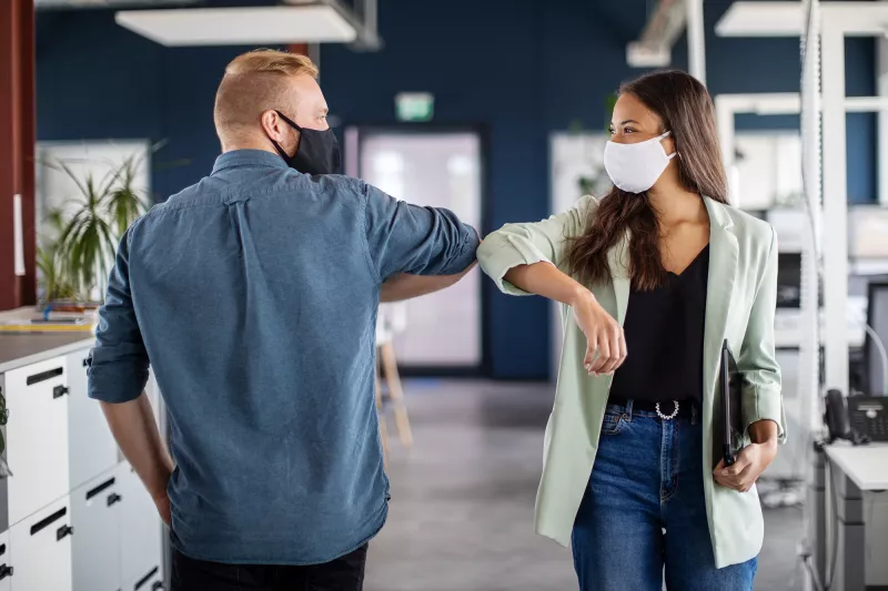 co-workers elbowing hello in the office while wear facemasks
