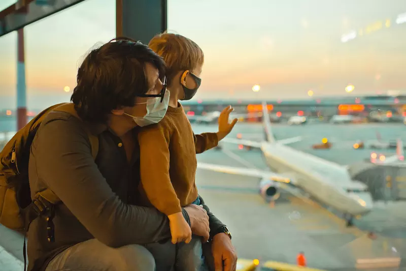 Father and son watch planes at the airport before boarding wearing face masks