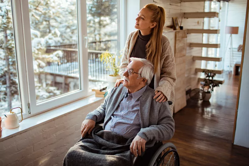 Caregiver Looks Out the Window with a Senior Patient at the Newly Fallen Snow.