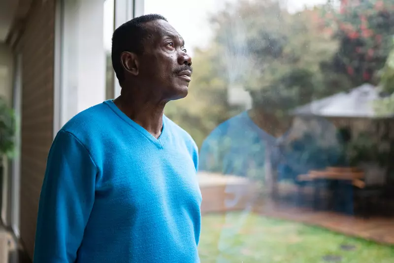 An African American Man Looks Out a Window into the Forest. 