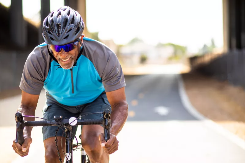 A Middle Aged Man Rides a Bicycle on a Road while Dressed in Typical Cyclist Attire.