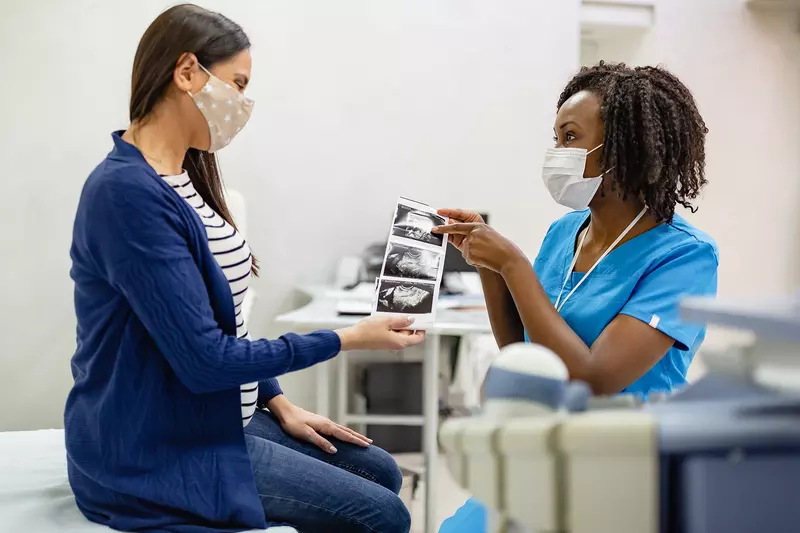 A Woman Looks Over The Sonogram of Her Baby with Her Physician.
