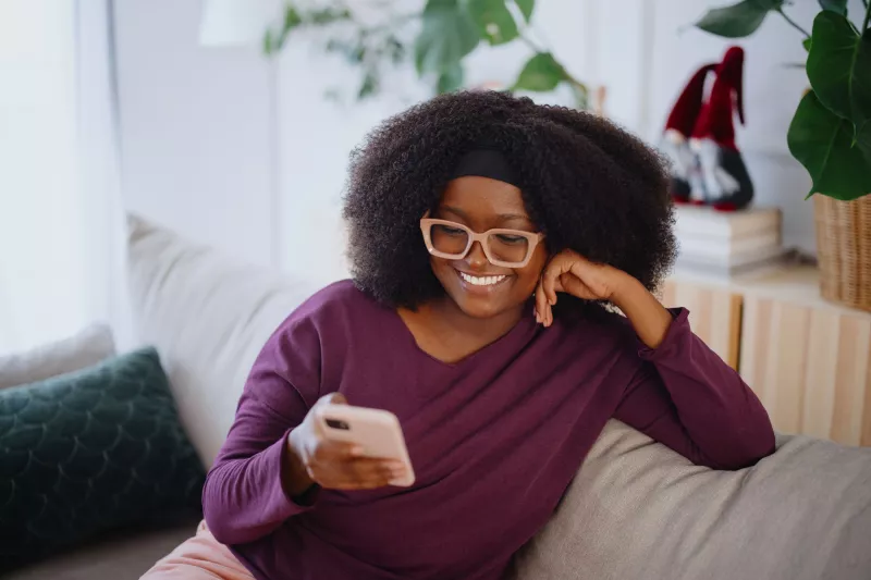 A Woman Smiles as She Reads Her Cell Phone on the Couch at Home.