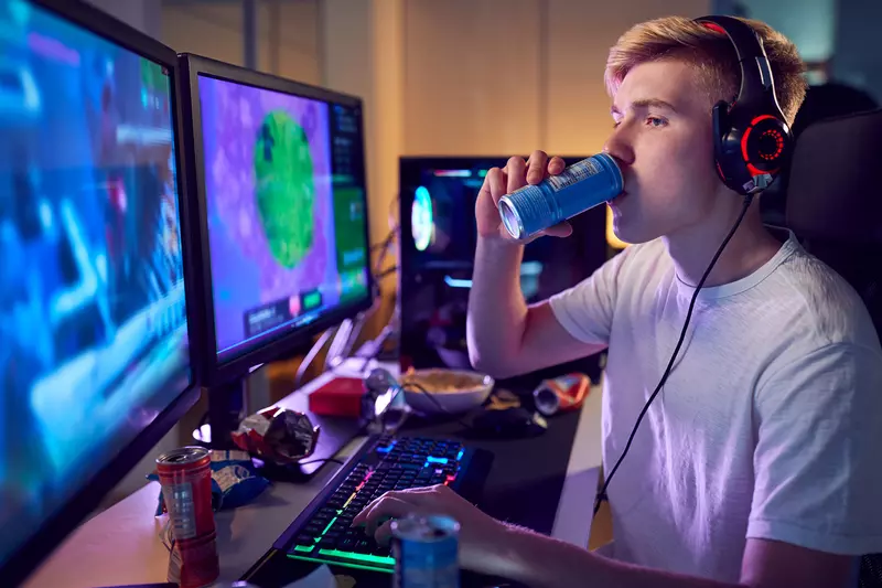 Teenager Drinks an Energy Drink While Playing Video Games with A Headset on.