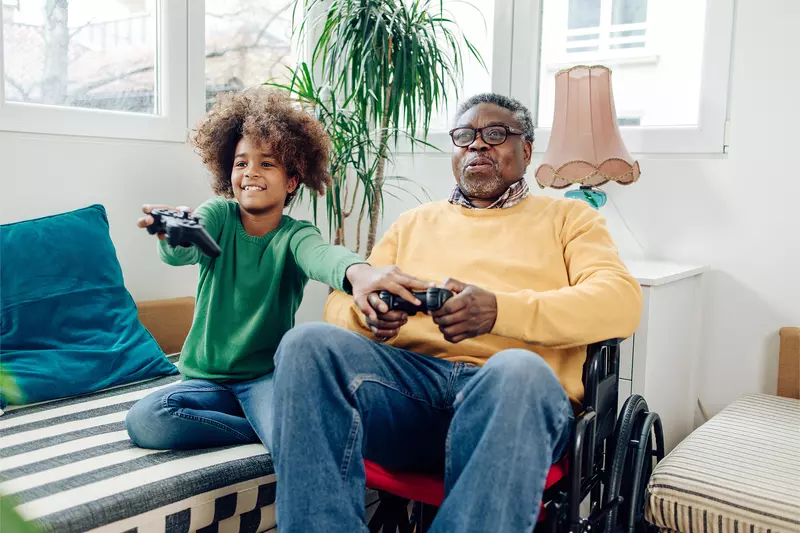 A Grandfather in a Wheelchair Plays Video Games with His Grandson who is Teaching Him How To Play.