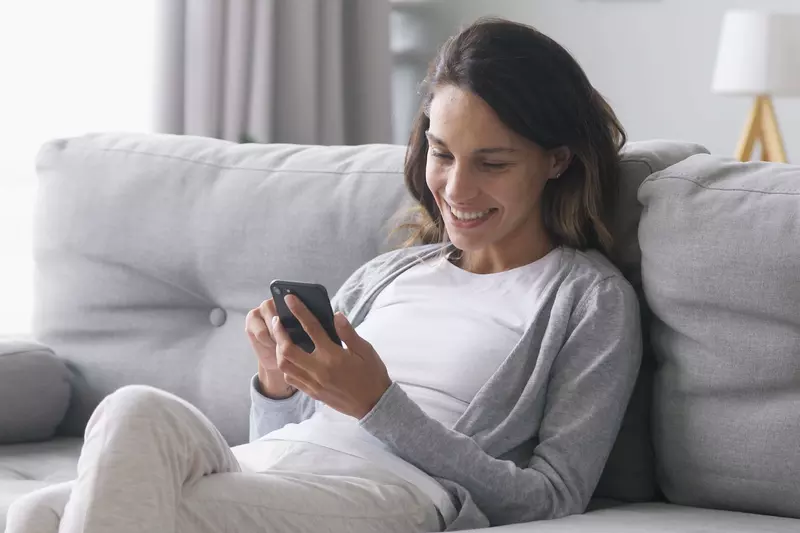 A Woman Sits on Her Couch and Uses Her Smartphone.