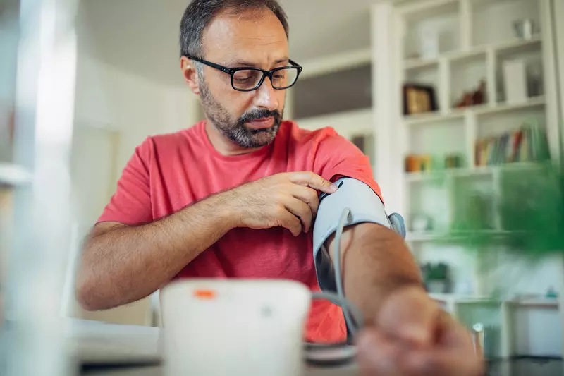 A Middle Aged Man Wearing Glasses Puts on a Blood Pressure Cuff to Take His Blood Pressure.