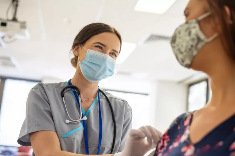 A Nurse Smiles as She Prepares a Patient for an Injection.