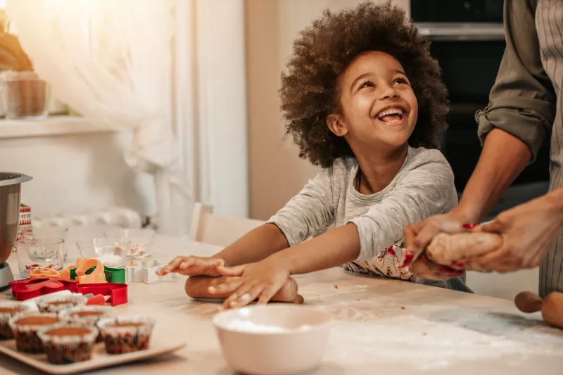 A Young Child Helps Their Parent Roll Out Dough to Make Muffins