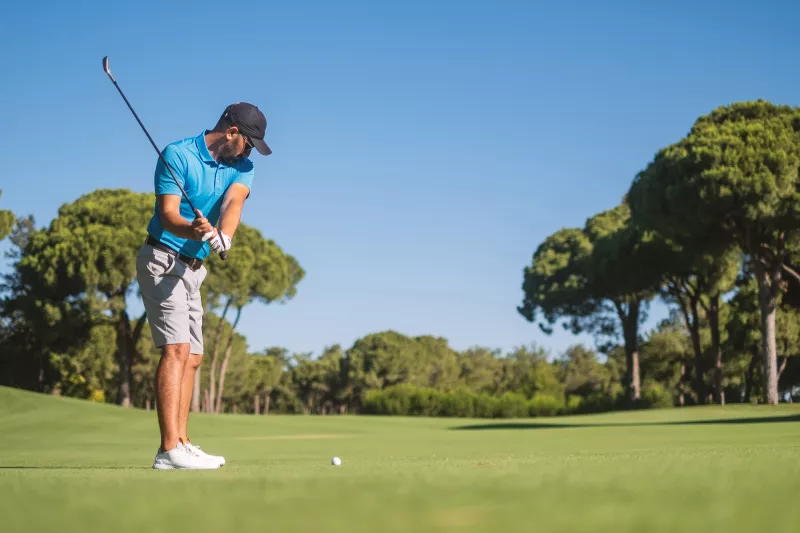 A Man Playing Golf with His Club in the Back Swing of His Approach to the Green.