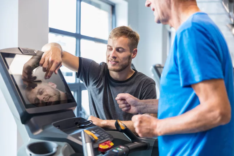 A Trainer Sets Up a Treadmill for a Patient