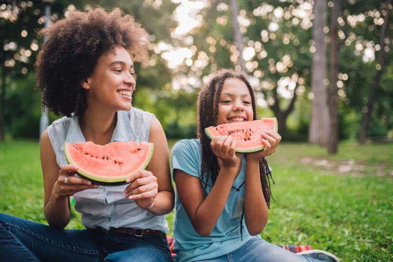 A Mother and Daughter Sit at a Picnic Enjoying Fruit