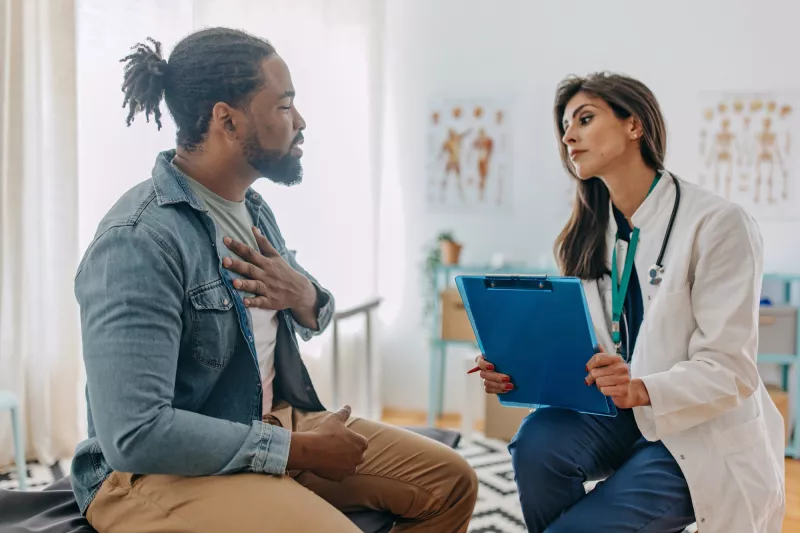 A Patient Holds His Hand to His Chest as He Consults with His Physician in a Doctor's Office.