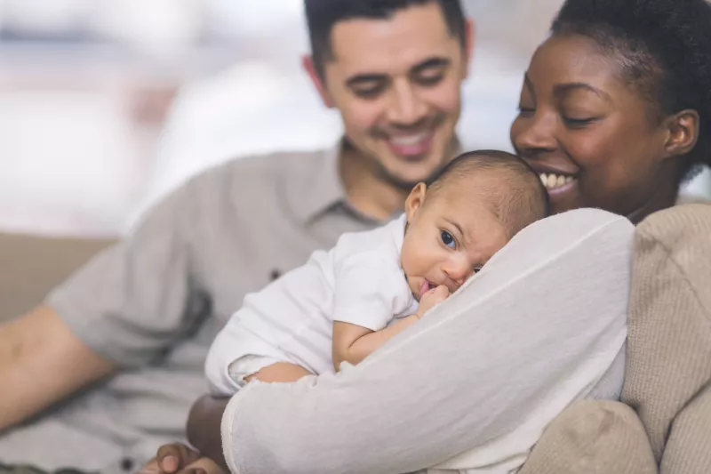 A New Mom Holds Her Baby While While Her Husband Smiles