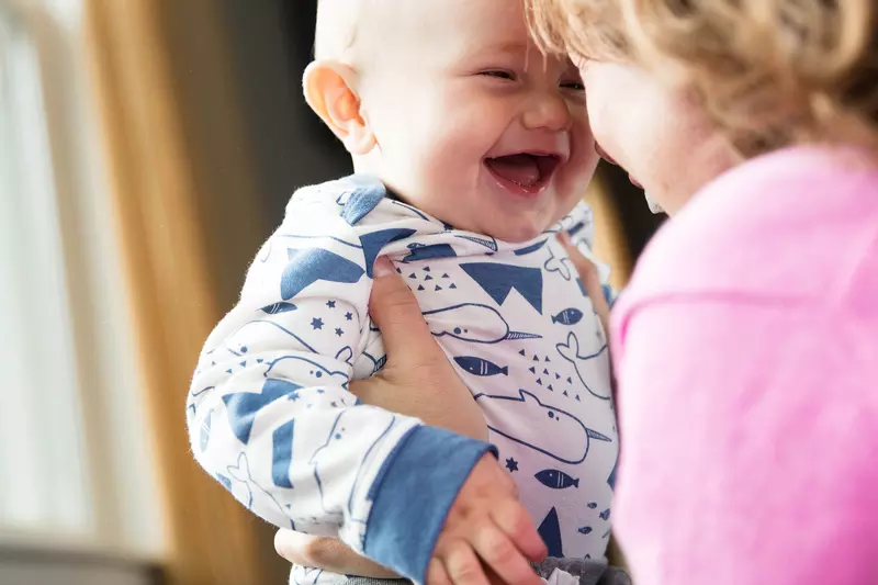 Baby laughing while his mother is holding him.