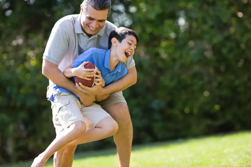 A father and son play football outdoors.