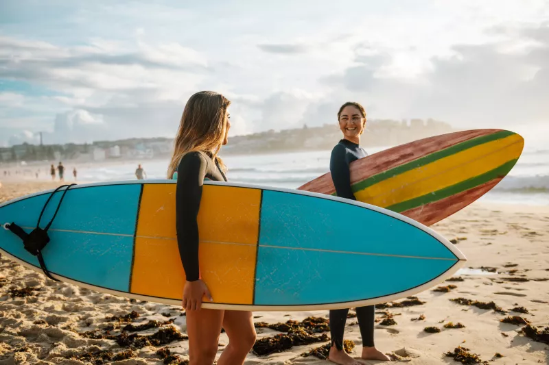 Two healthy women enjoy surfing at the beach.