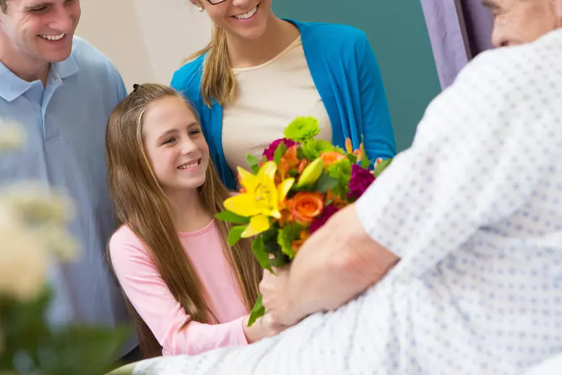 Family with child giving flowers to a hospital patient