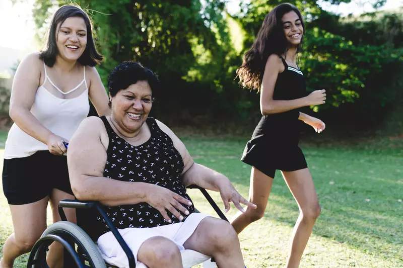 A woman in a wheelchair enjoys the outdoors with her daughters during the summer.