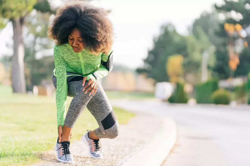 A woman checking her ankle during her run.