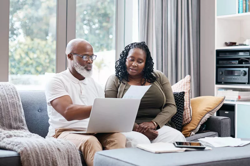 Man and woman reviewing paperwork with computer on lap