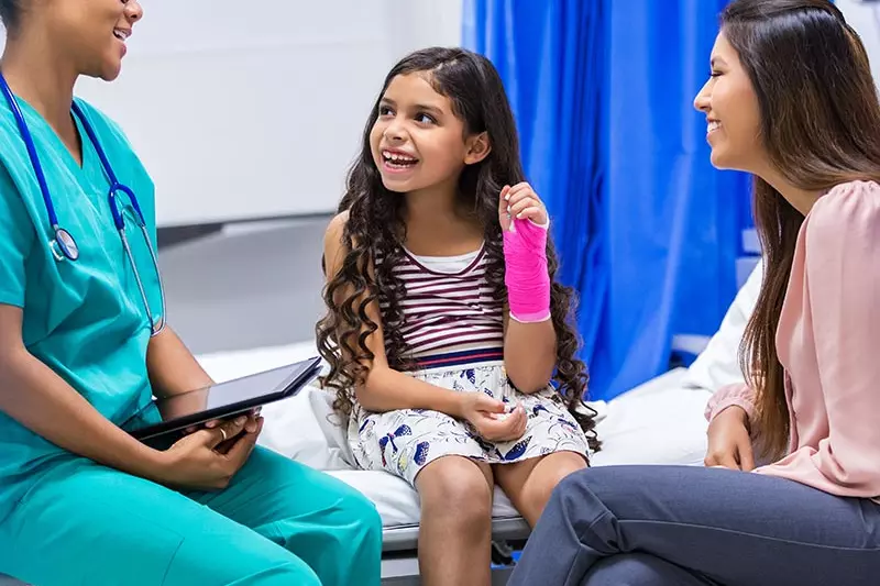 Child with a cast on her arm is sitting with a doctor and her mother