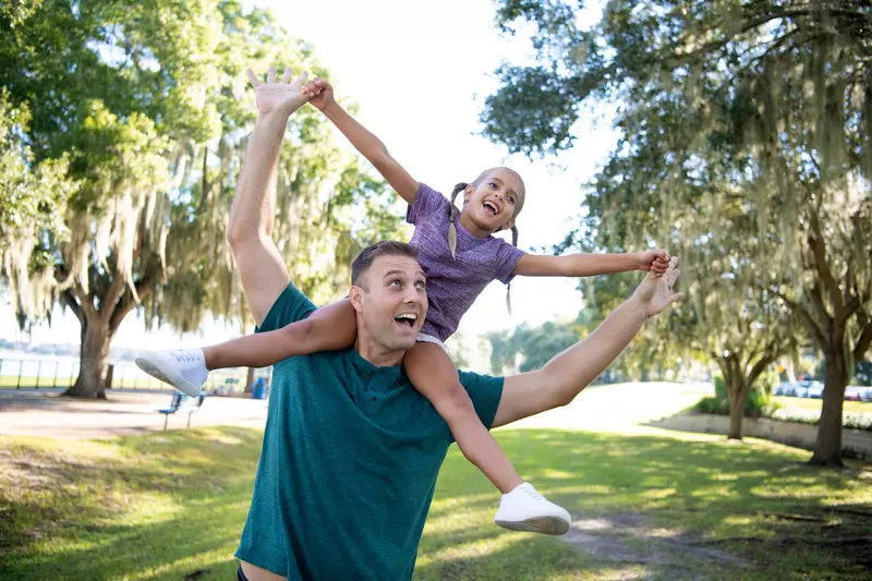 A Father Carries His Daughter on His Shoulders as they Play in a Park