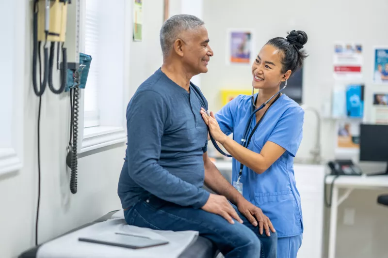 An older Hispanic man gets examined by a nurse.