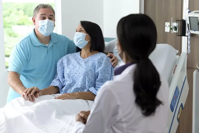 Couple in hospital room wearing masks talking to doctor