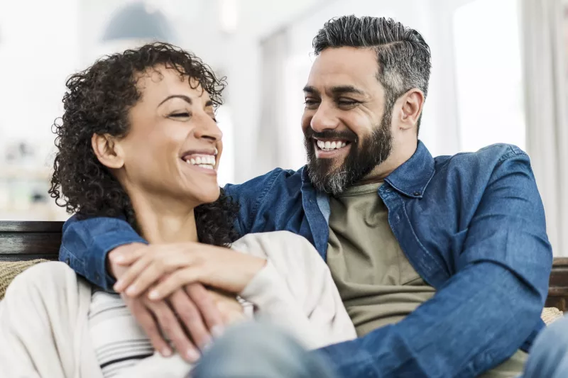 A couple laughs together on the couch.