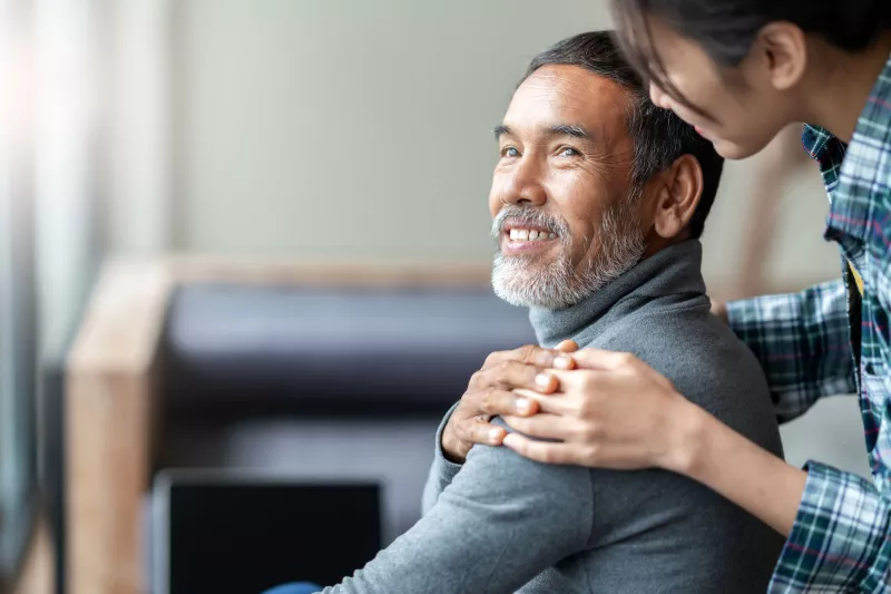 A daughter hugs her father from behind.