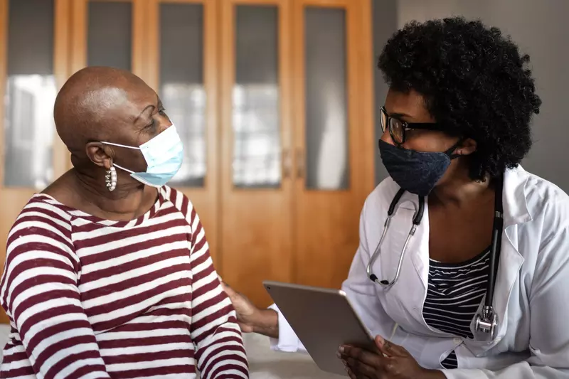 A doctor and patient discuss health care while wearing masks.