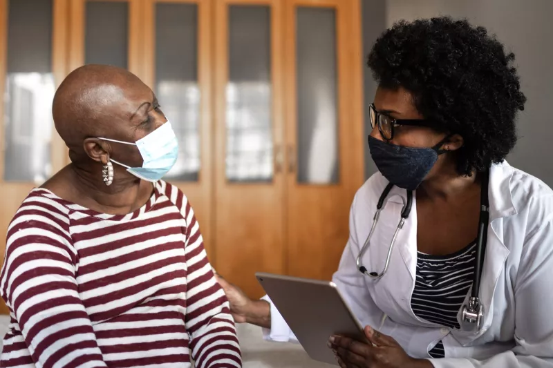 A doctor and patient discuss health care while wearing masks.
