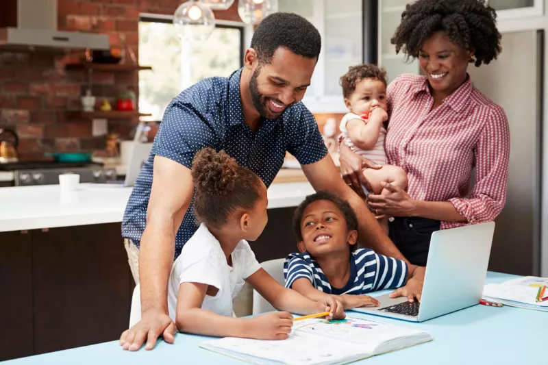 Photo of a family standing at a laptop making plans and smiling.