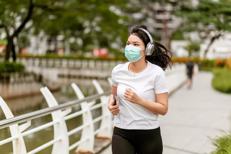 Woman running in a park outside while wearing a mask.