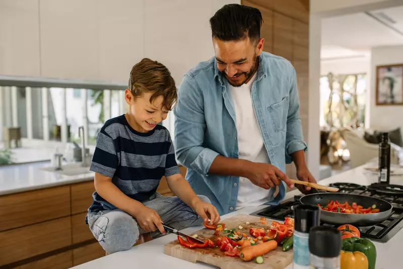 A father an son laugh together while preparing a healthy meal.