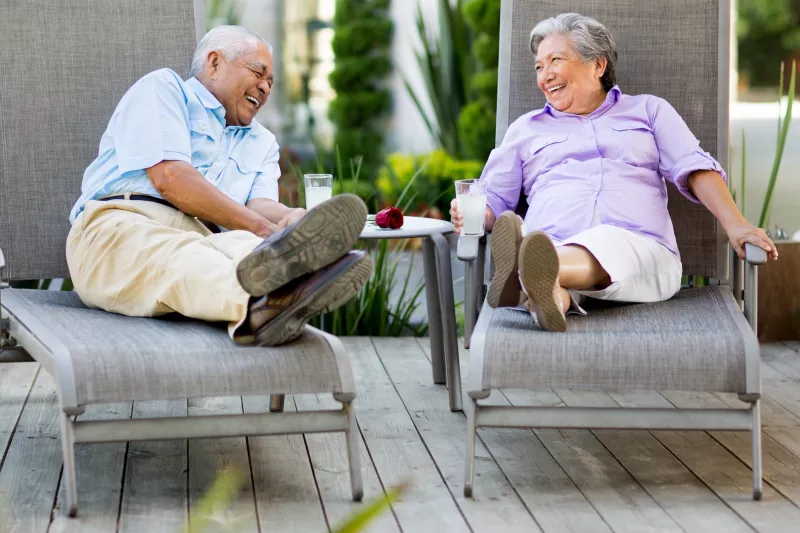 A couple chatting and laughing in lounge chairs outdoors.