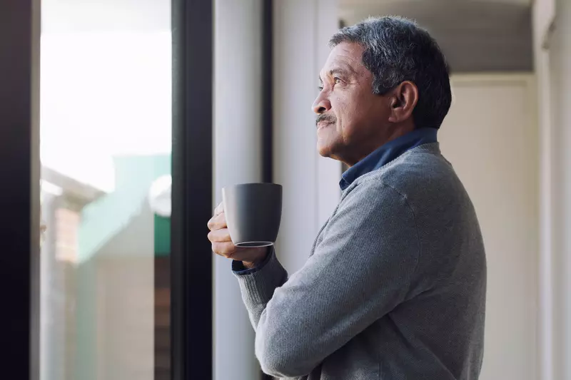 A man drinking coffee while looking outside from his window