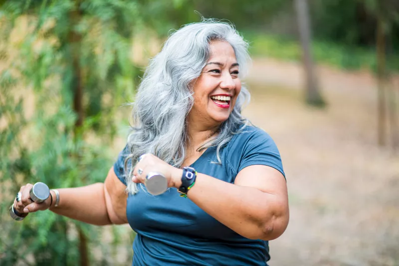 An overweight senior hispanic woman uses weights while she exercises
