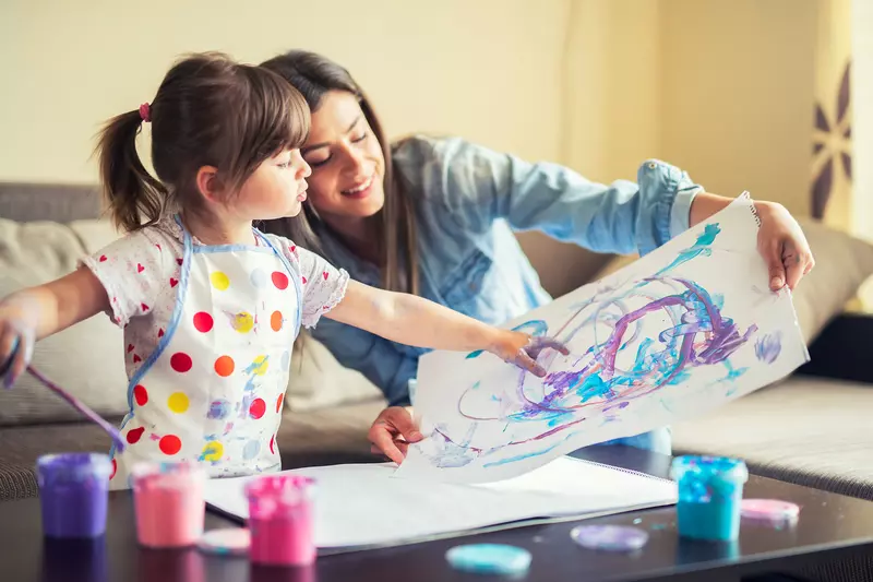 A mother and young daughter painting together. 