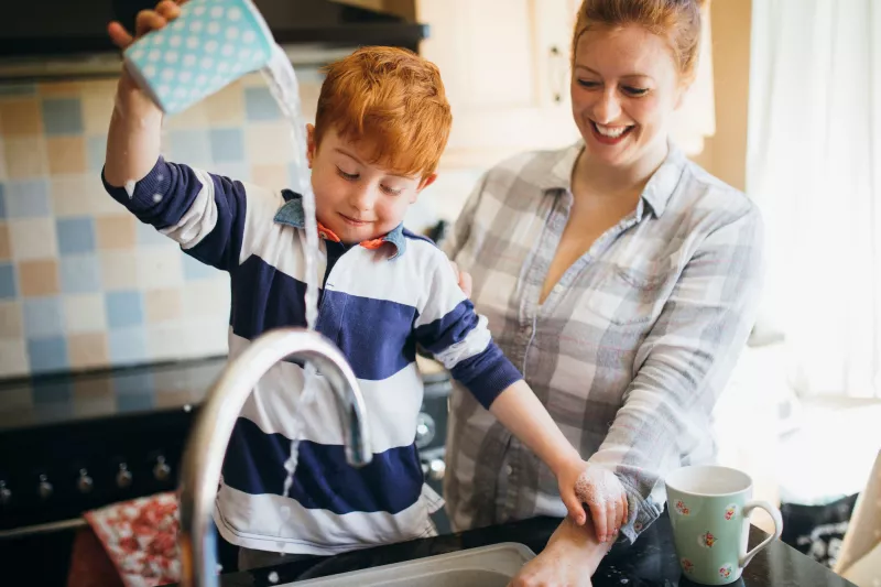 A mom and son wash dishes together.