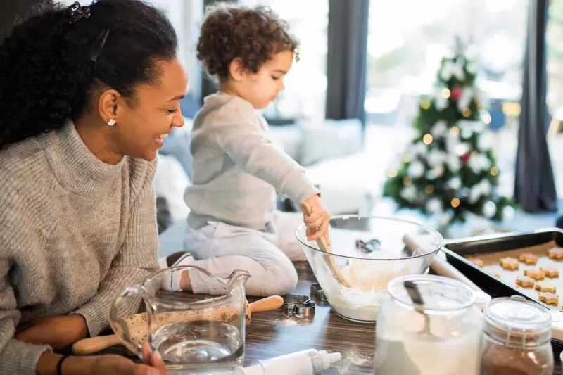 A mom and her toddler bake Christmas cookies together.